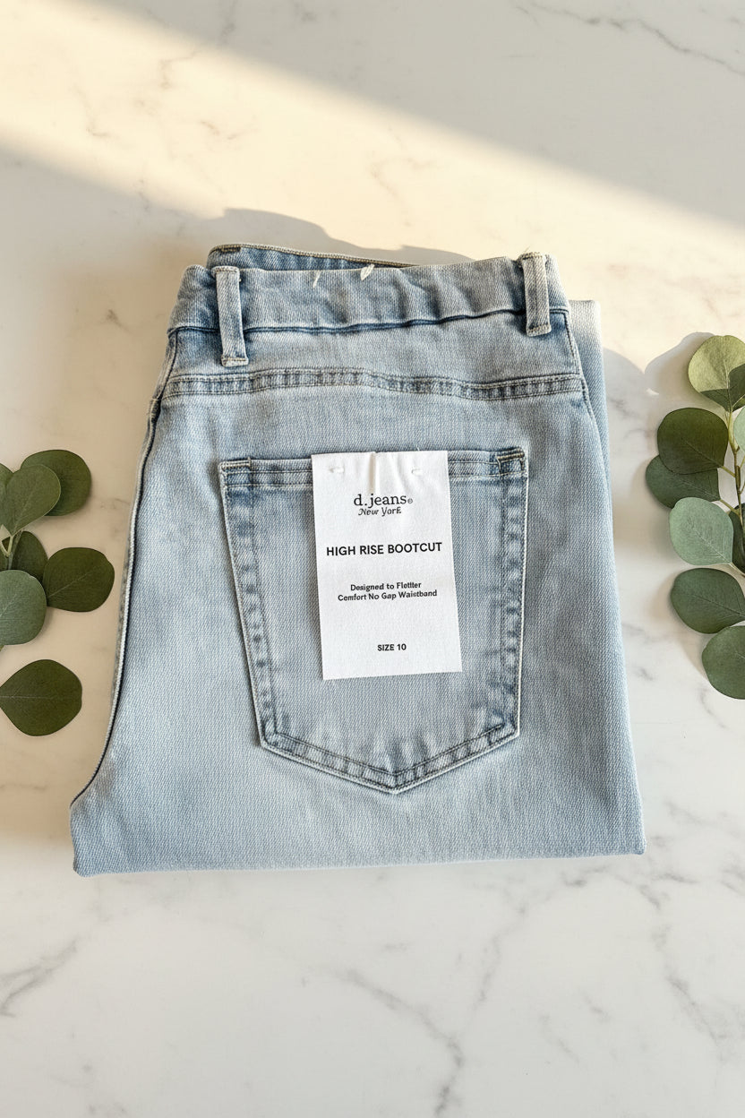 Folded pair of light blue jeans with a label on a marble surface with green leaves.